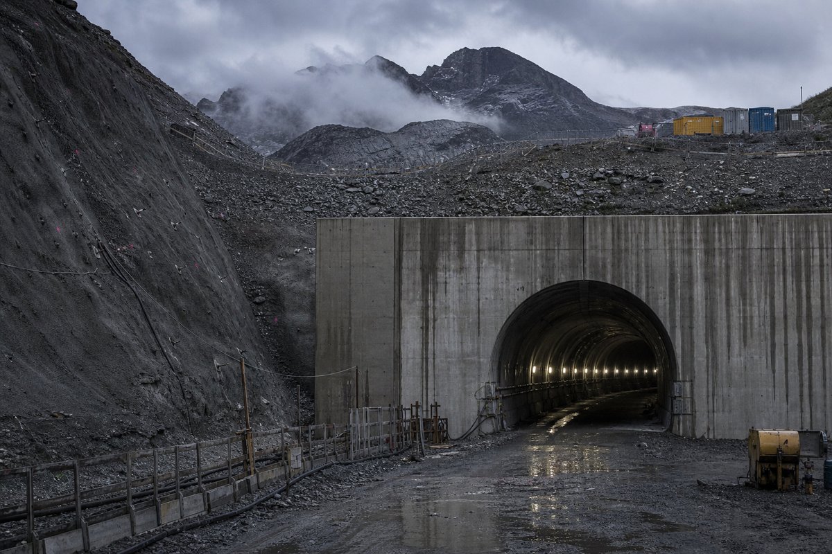Archival-feeling engineering scene, dim and documentary: a mountainous transport corridor, under low grey cloud, shot at 85mm from a distance. (AI-generated image)