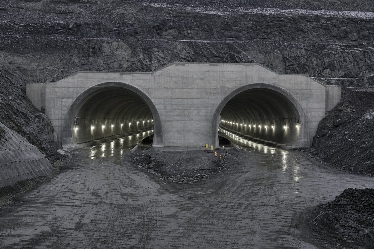 Two parallel tunnel bores diverging behind a shared portal wall, cold LED lighting, in flat overcast light, shot at 85mm from a distance. Frame 272. (AI-generated image)