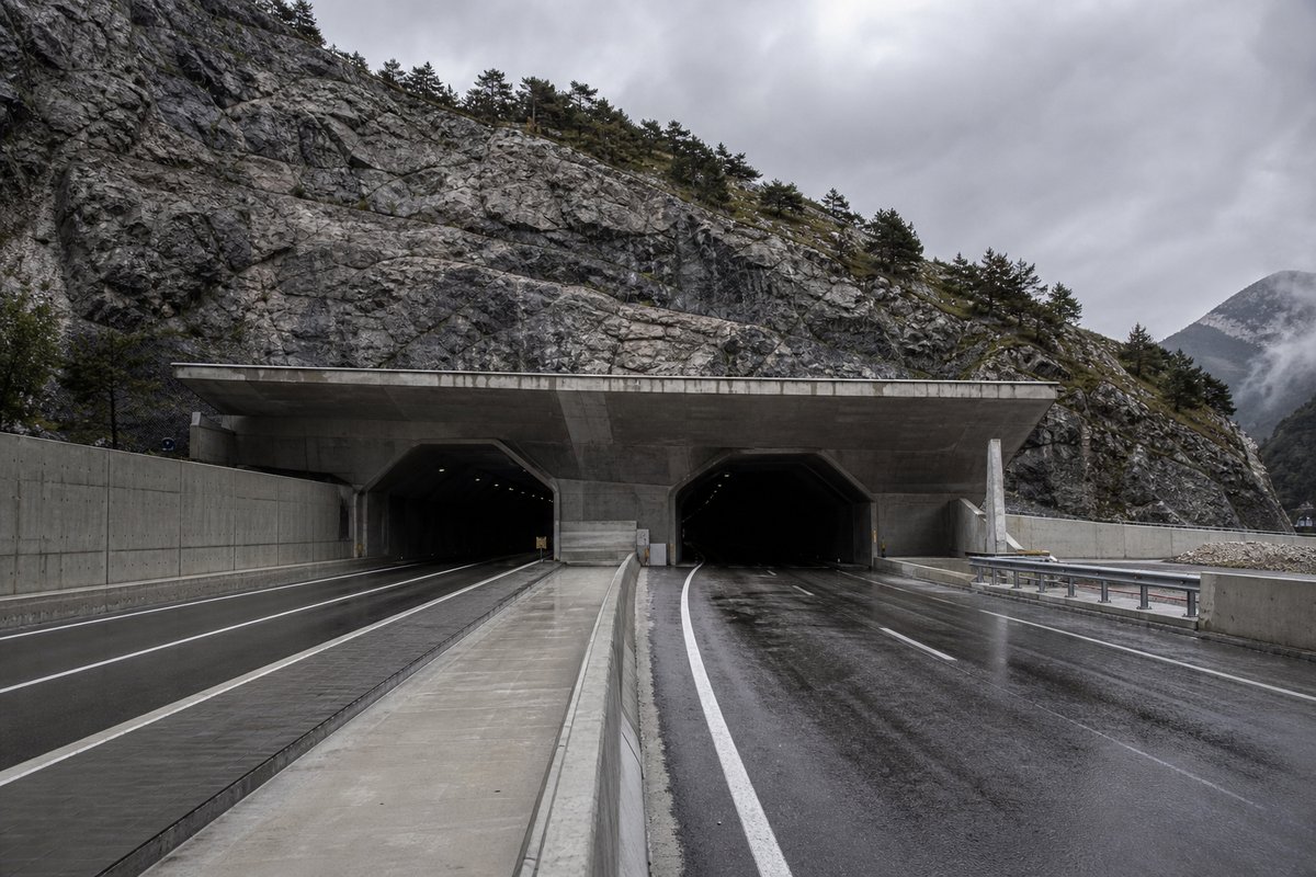 Twin motorway portals under a projecting concrete canopy on a limestone ridge, under low grey cloud, shot at 35mm. Frame 788. (AI-generated image)