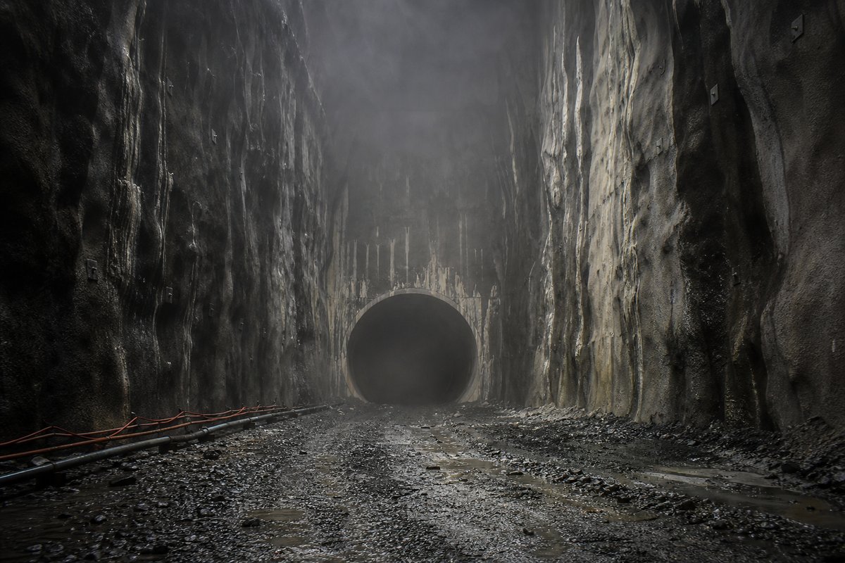 Deep rock cutting terminating in a portal, shotcrete walls streaked with seepage, in drifting mist, shot at 35mm. Frame 42. (AI-generated image)