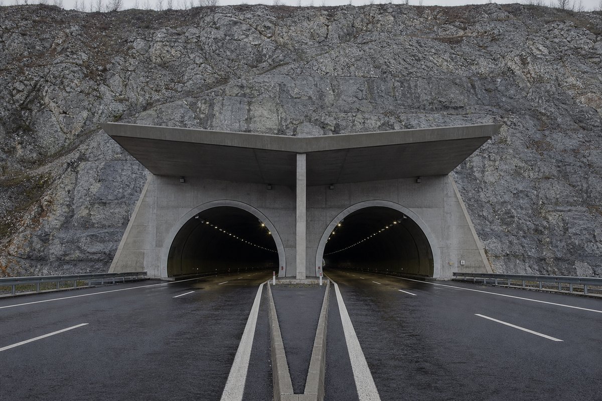 Twin motorway portals under a projecting concrete canopy on a limestone ridge, in flat overcast light, a dead-centre symmetrical composition. Frame 3. (AI-generated image)