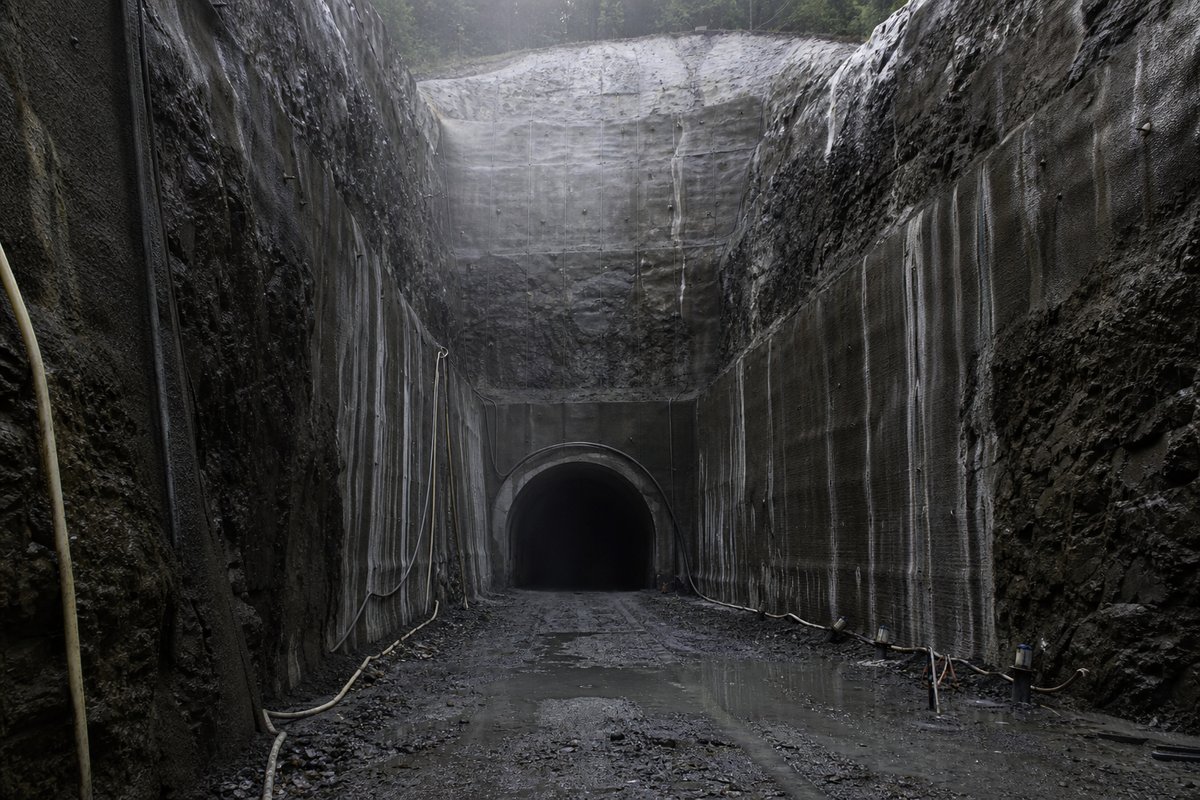Deep rock cutting terminating in a portal, shotcrete walls streaked with seepage, in drifting mist, shot at 50mm. Frame 862. (AI-generated image)