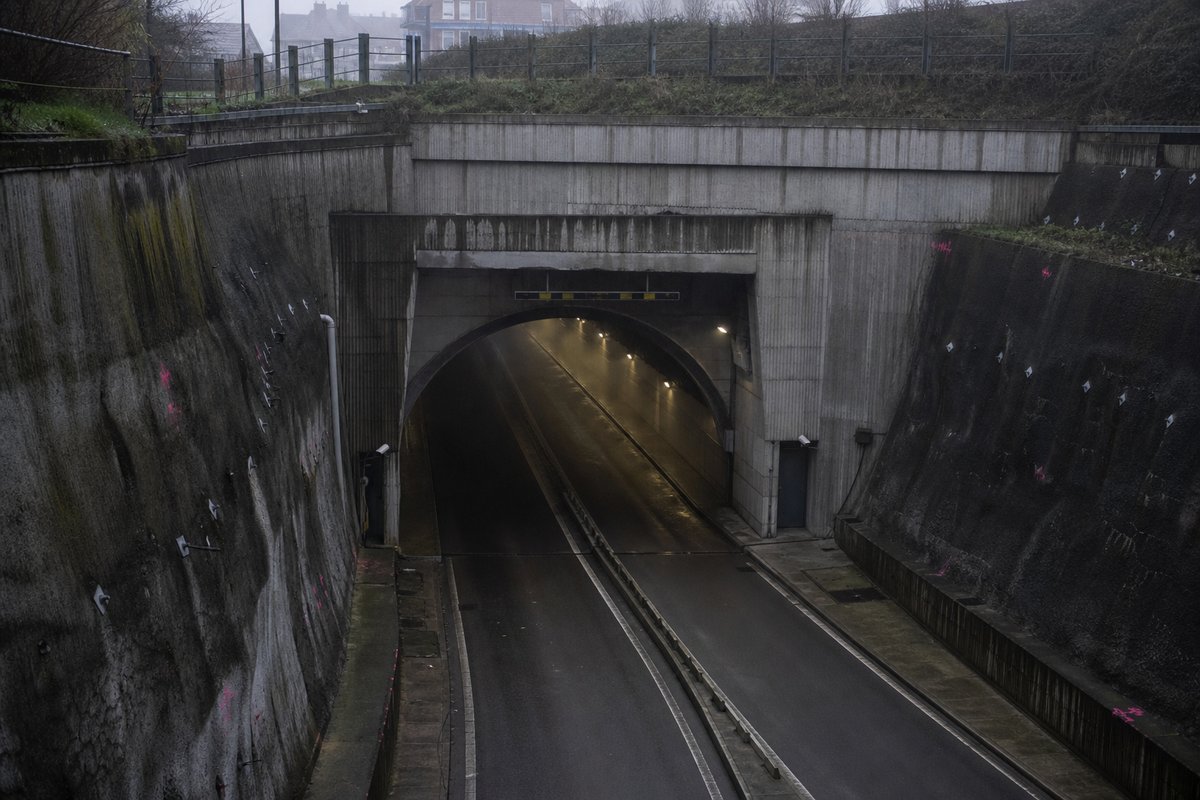 Road tunnel portal in Belgium: urban cutting with a 1960s concrete road tunnel entrance, in drifting mist, a slightly elevated three-quarter view. (AI-generated image)