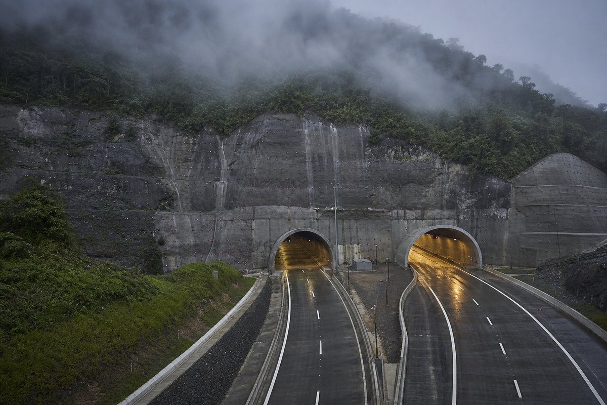 Road tunnel portal in Brazil: Atlantic rainforest escarpment with a motorway tunnel portal, under low grey cloud, a slightly elevated three-quarter view. (AI-generated image)