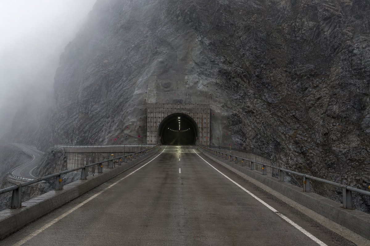 Road tunnel portal in Chile: Andes rock face with a road tunnel above a switchback, in thin morning fog, a dead-centre symmetrical composition. (AI-generated image)