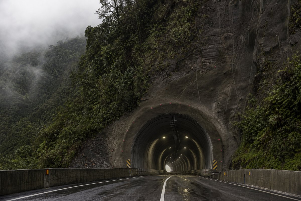 Road tunnel portal in Ecuador: Andean cloud forest with a road tunnel portal, in thin morning fog, shot at 50mm, compressed. (AI-generated image)