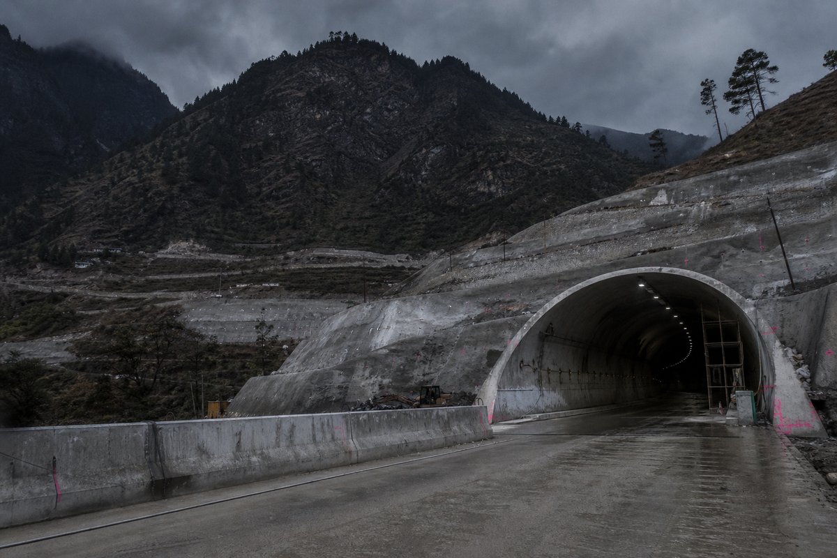 Road tunnel portal in India: Himalayan slope with terraced switchbacks and a new highway portal, under a heavy dark sky, shot at 35mm. (AI-generated image)