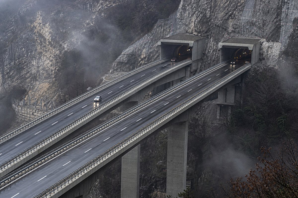 Motorway viaduct and tunnel portal in sequence along an autostrada in Italy: Apennine limestone ridge, twin concrete motorway portals with a projecting canopy, in drifting mist. (AI-generated image)