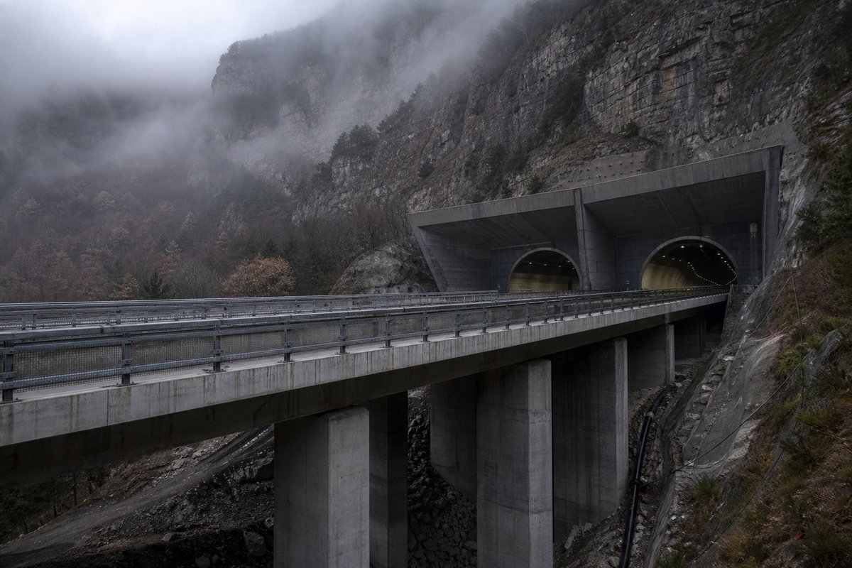 Motorway viaduct and tunnel portal in sequence along an autostrada in Italy: Apennine limestone ridge, twin concrete motorway portals with a projecting canopy, in drifting mist. (AI-generated image)