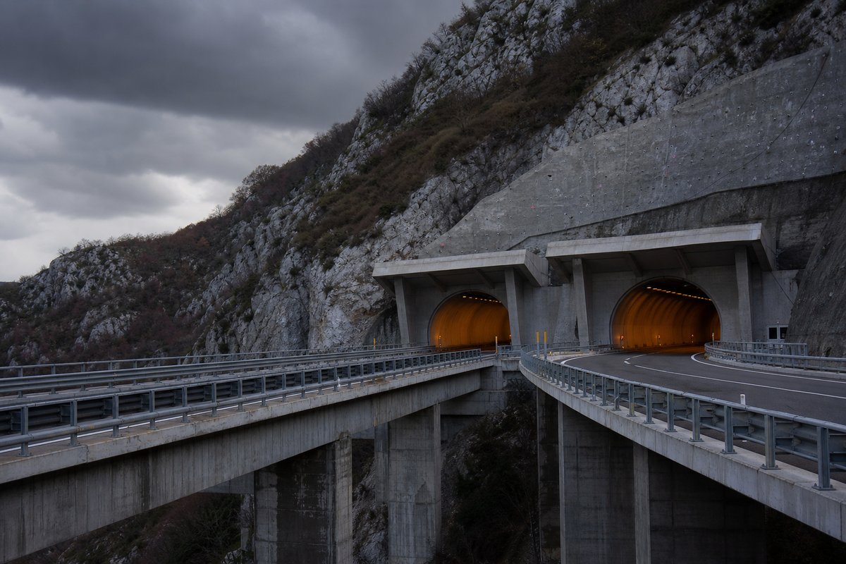 Motorway viaduct and tunnel portal in sequence along an autostrada in Italy: Apennine limestone ridge, twin concrete motorway portals with a projecting canopy. (AI-generated image)