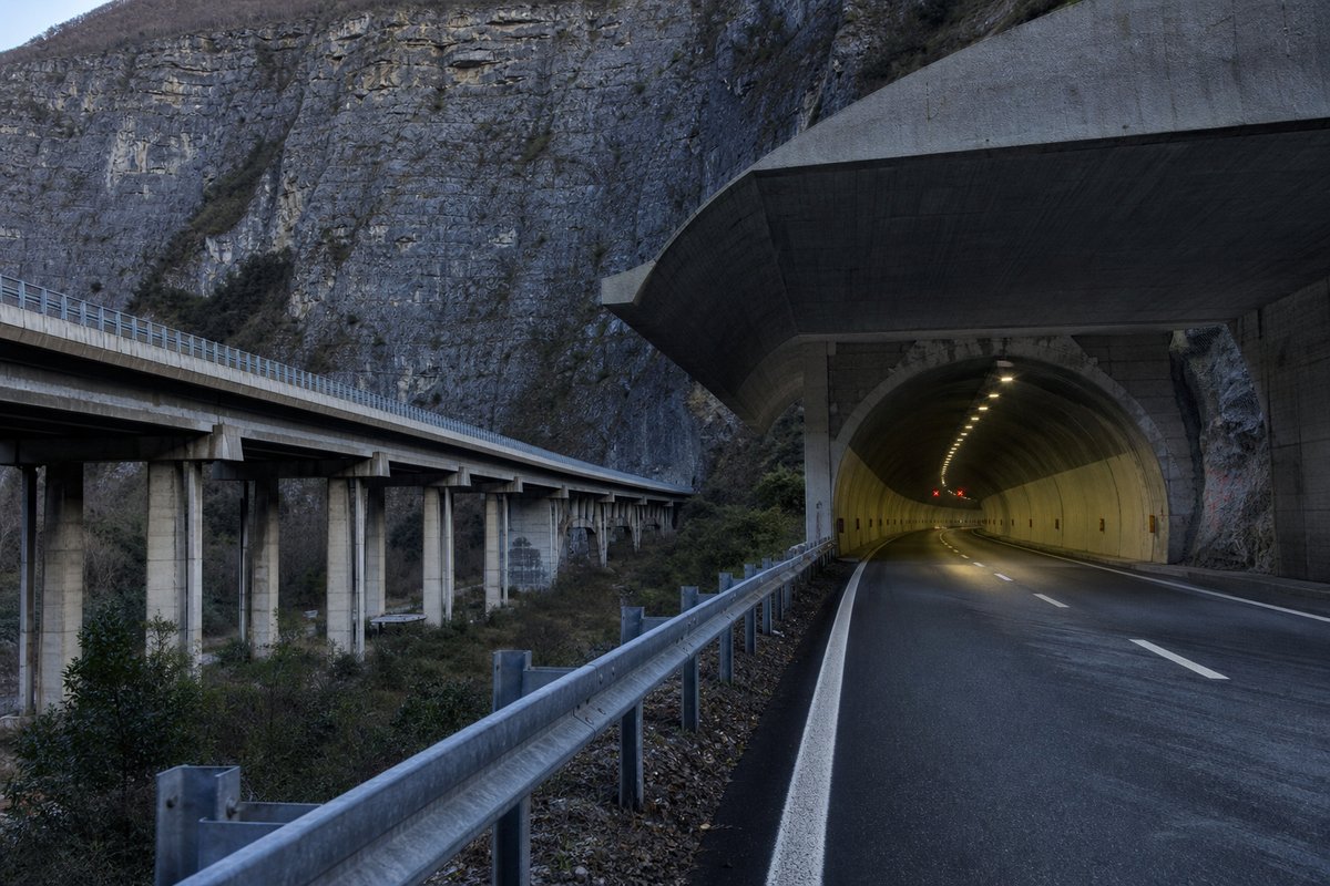 Motorway viaduct and tunnel portal in sequence along an autostrada in Italy: Apennine limestone ridge, twin concrete motorway portals with a projecting canopy, in cold clear light. (AI-generated image)