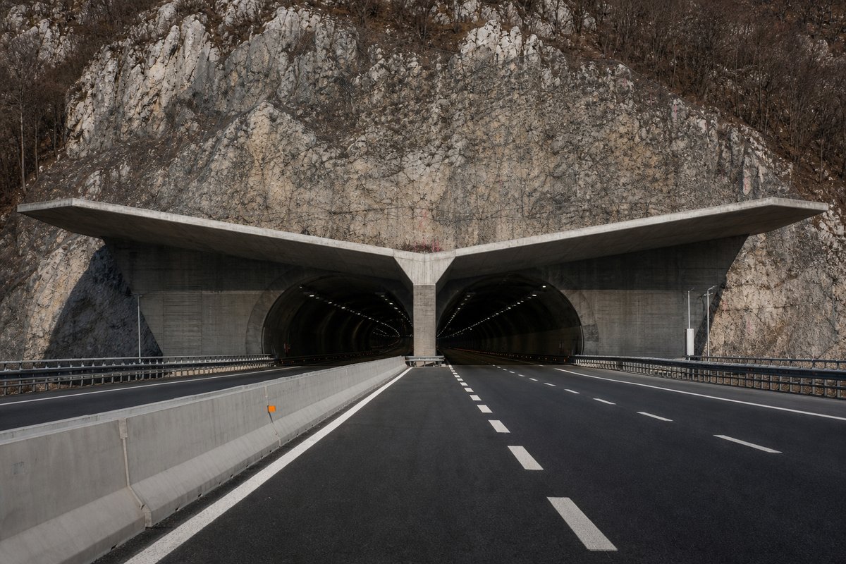 Motorway viaduct and tunnel portal in sequence along an autostrada in Italy: Apennine limestone ridge, twin concrete motorway portals with a projecting canopy. (AI-generated image)