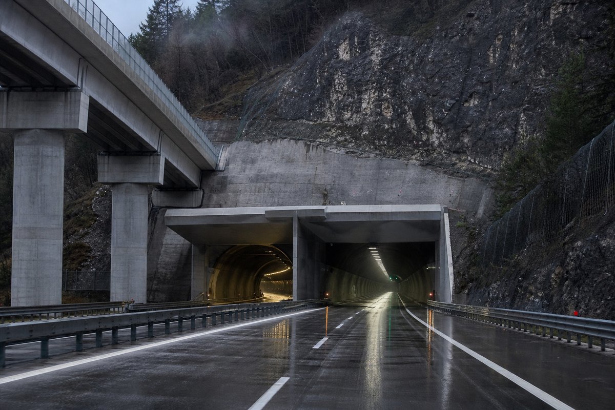 Motorway viaduct and tunnel portal in sequence along an autostrada in Italy: Apennine limestone ridge, twin concrete motorway portals with a projecting canopy, after rain. (AI-generated image)