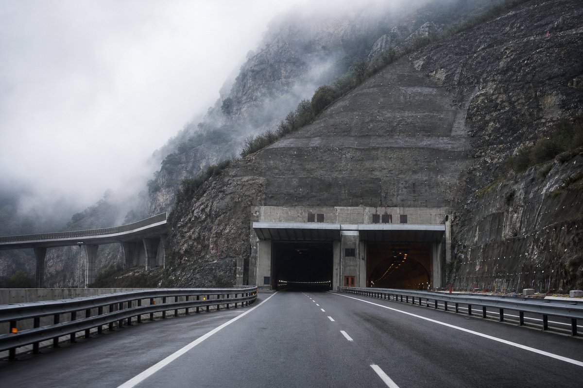 Motorway viaduct and tunnel portal in sequence along an autostrada in Italy: Apennine limestone ridge, twin concrete motorway portals with a projecting canopy, in drifting mist. (AI-generated image)
