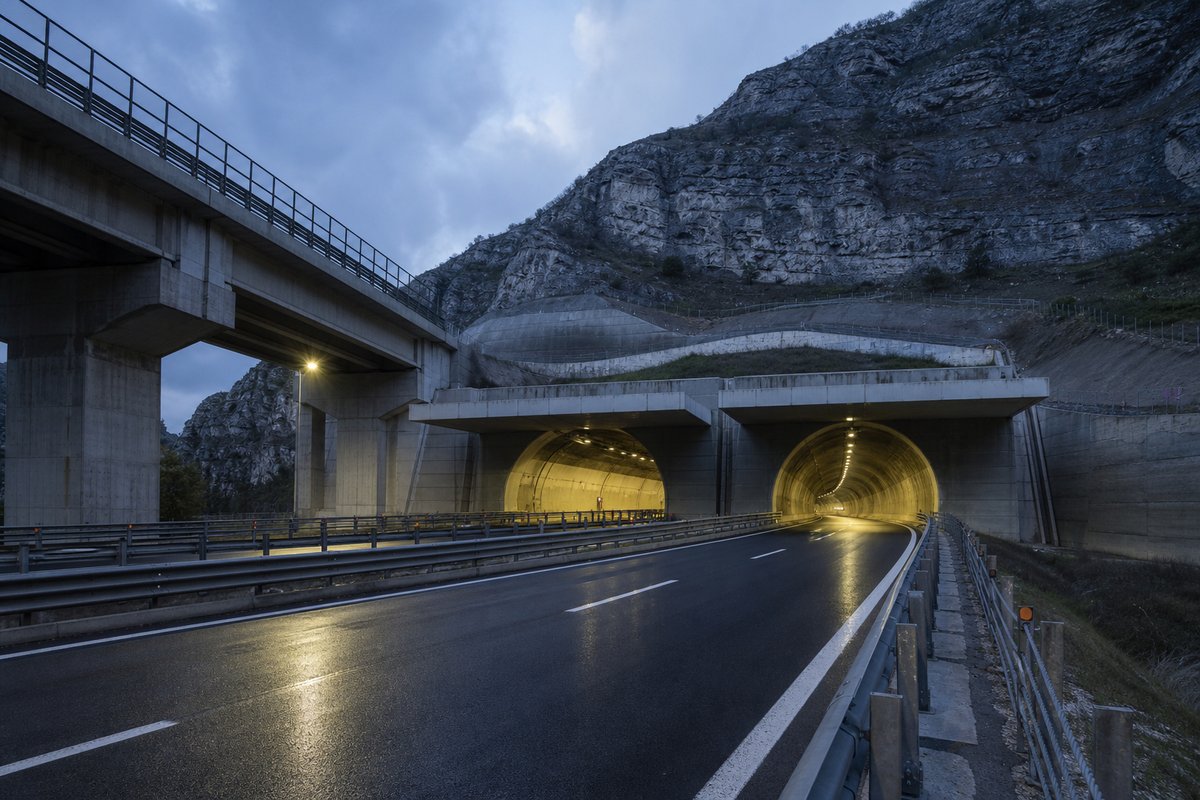 Motorway viaduct and tunnel portal in sequence along an autostrada in Italy: Apennine limestone ridge, twin concrete motorway portals with a projecting canopy. (AI-generated image)