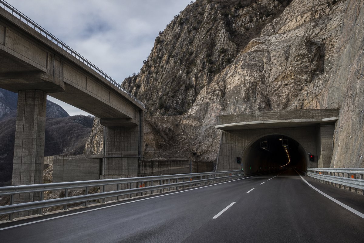 Motorway viaduct and tunnel portal in sequence along an autostrada in Italy: Apennine limestone ridge, twin concrete motorway portals with a projecting canopy. (AI-generated image)