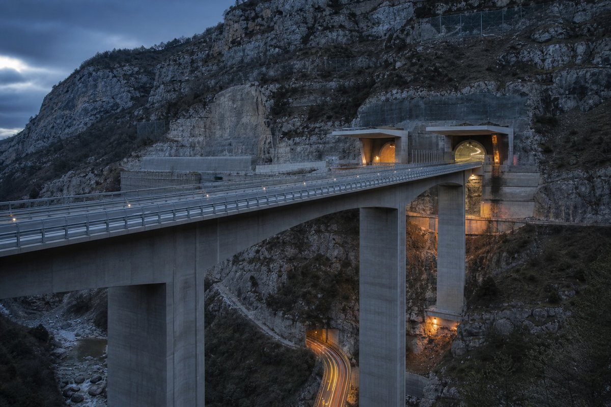 Long concrete box-girder viaduct on tall piers, seen from below in Italy: Apennine limestone ridge, twin concrete motorway portals with a projecting canopy. (AI-generated image)