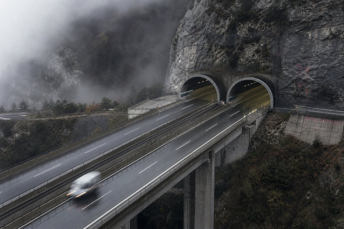Motorway viaduct and tunnel portal in sequence along an autostrada in Italy: Apennine limestone ridge, twin concrete motorway portals with a projecting canopy, in drifting mist. (AI-generated image)