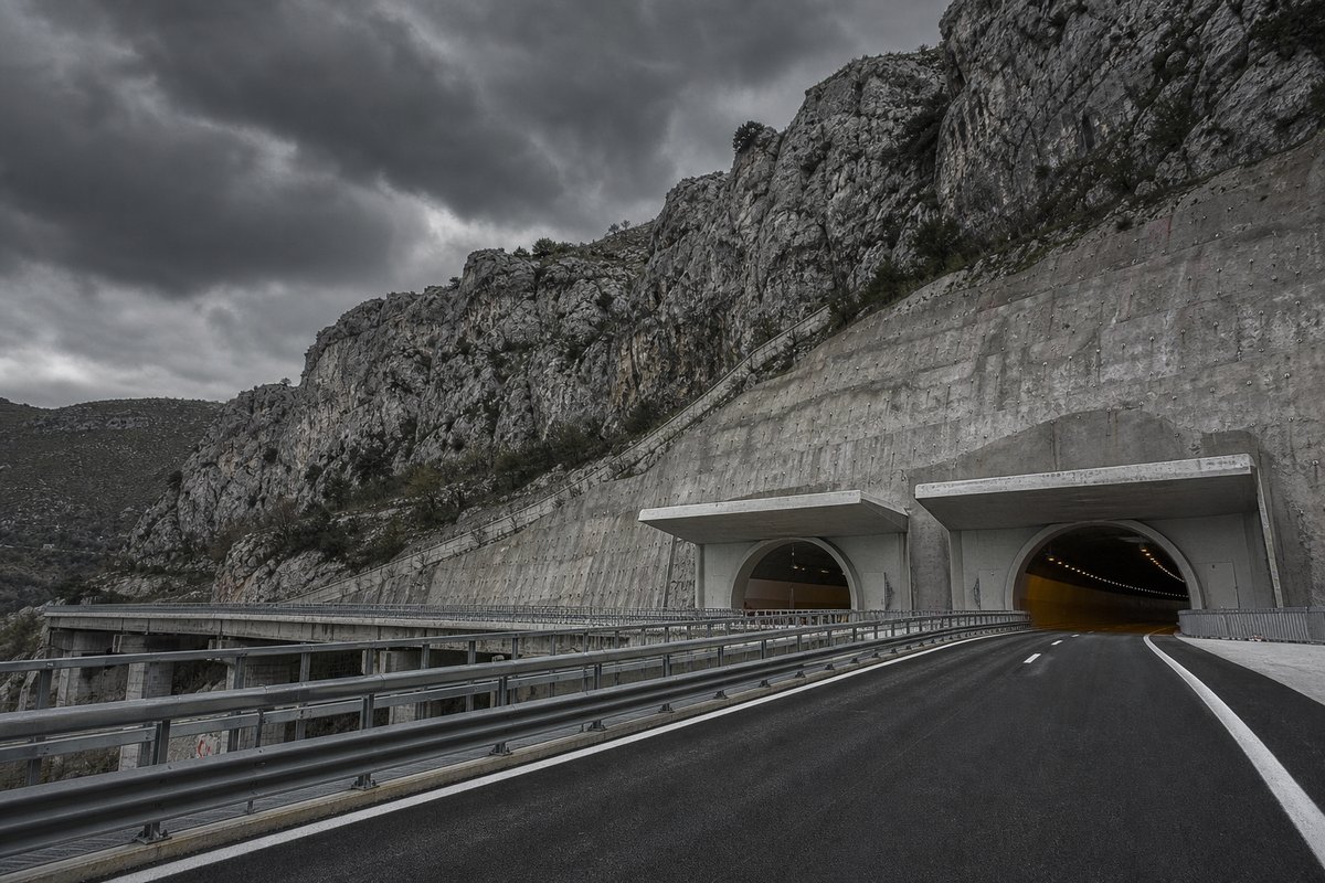 Motorway viaduct and tunnel portal in sequence along an autostrada in Italy: Apennine limestone ridge, twin concrete motorway portals with a projecting canopy. (AI-generated image)