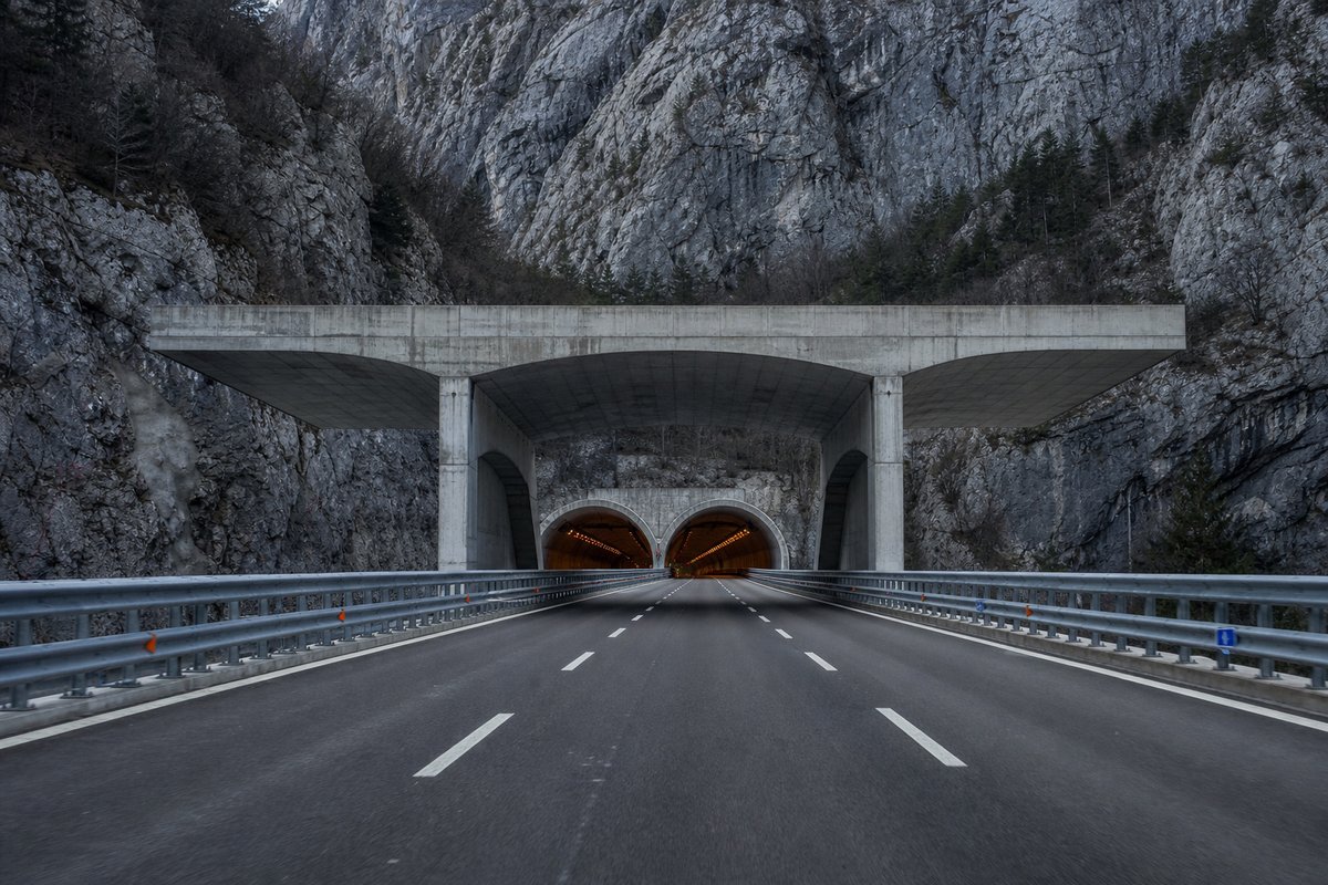 Motorway viaduct and tunnel portal in sequence along an autostrada in Italy: Apennine limestone ridge, twin concrete motorway portals with a projecting canopy, in cold clear light. (AI-generated image)