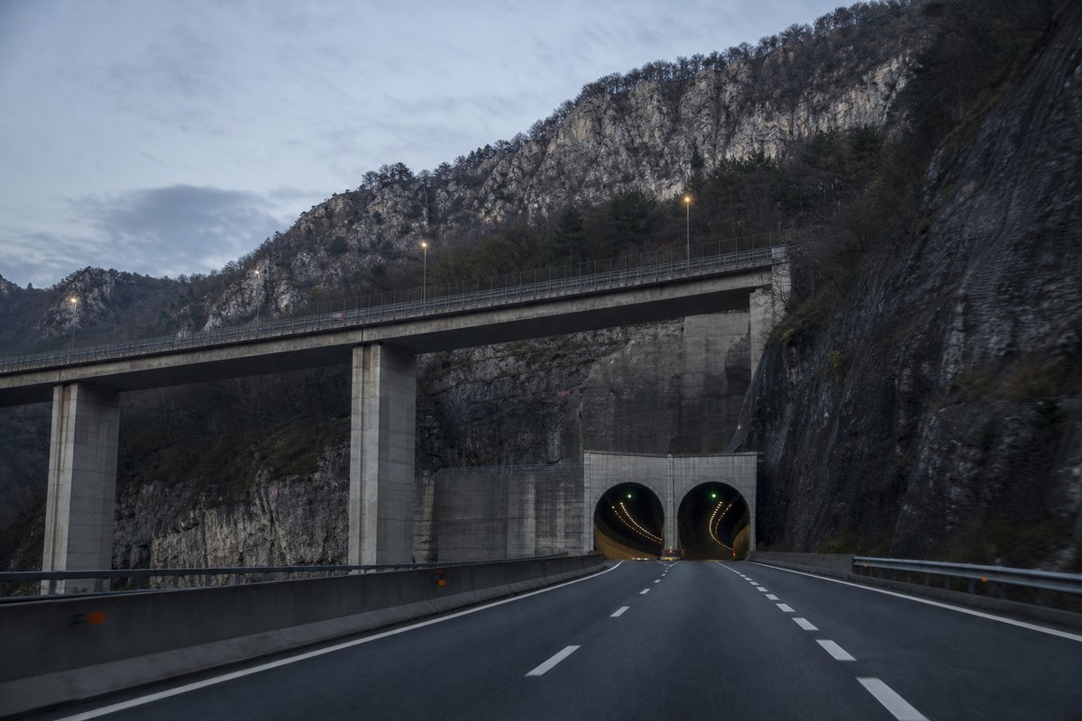 Motorway viaduct and tunnel portal in sequence along an autostrada in Italy: Apennine limestone ridge, twin concrete motorway portals with a projecting canopy. (AI-generated image)