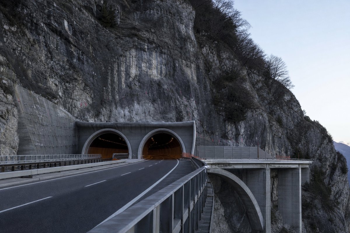 Motorway viaduct and tunnel portal in sequence along an autostrada in Italy: Apennine limestone ridge, twin concrete motorway portals with a projecting canopy, in cold clear light. (AI-generated image)