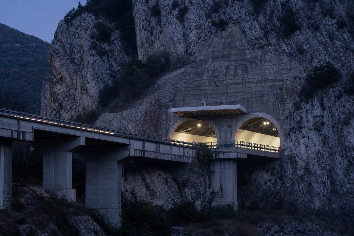Motorway viaduct and tunnel portal in sequence along an autostrada in Italy: Apennine limestone ridge, twin concrete motorway portals with a projecting canopy. (AI-generated image)