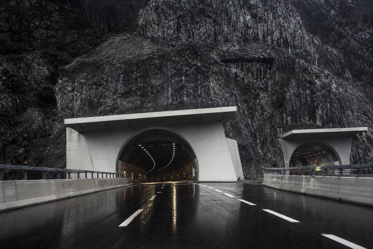 Motorway viaduct and tunnel portal in sequence along an autostrada in Italy: Apennine limestone ridge, twin concrete motorway portals with a projecting canopy, after rain. (AI-generated image)
