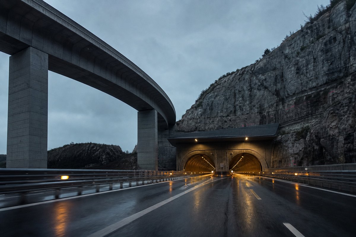 Motorway viaduct and tunnel portal in sequence along an autostrada in Italy: Apennine limestone ridge, twin concrete motorway portals with a projecting canopy. (AI-generated image)