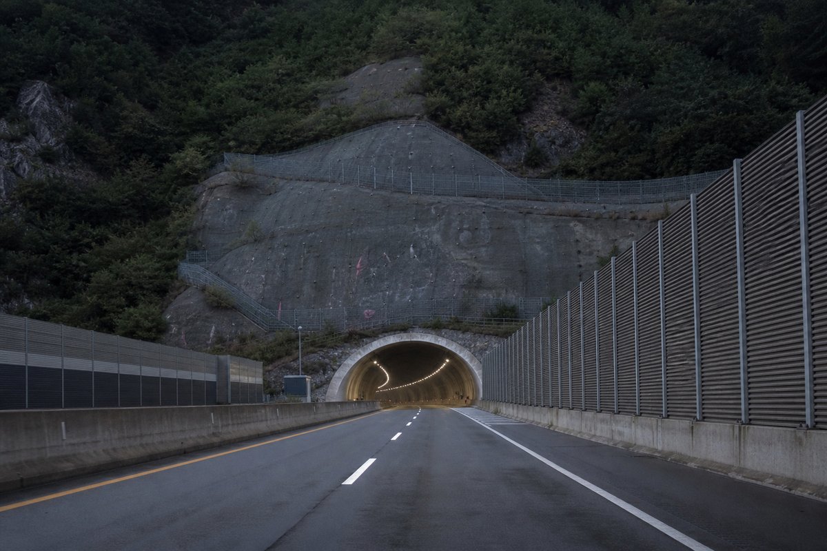 Road tunnel portal in South Korea: steep green ridge, a long expressway tunnel portal with sound walls, in cold clear light, shot at 35mm. (AI-generated image)