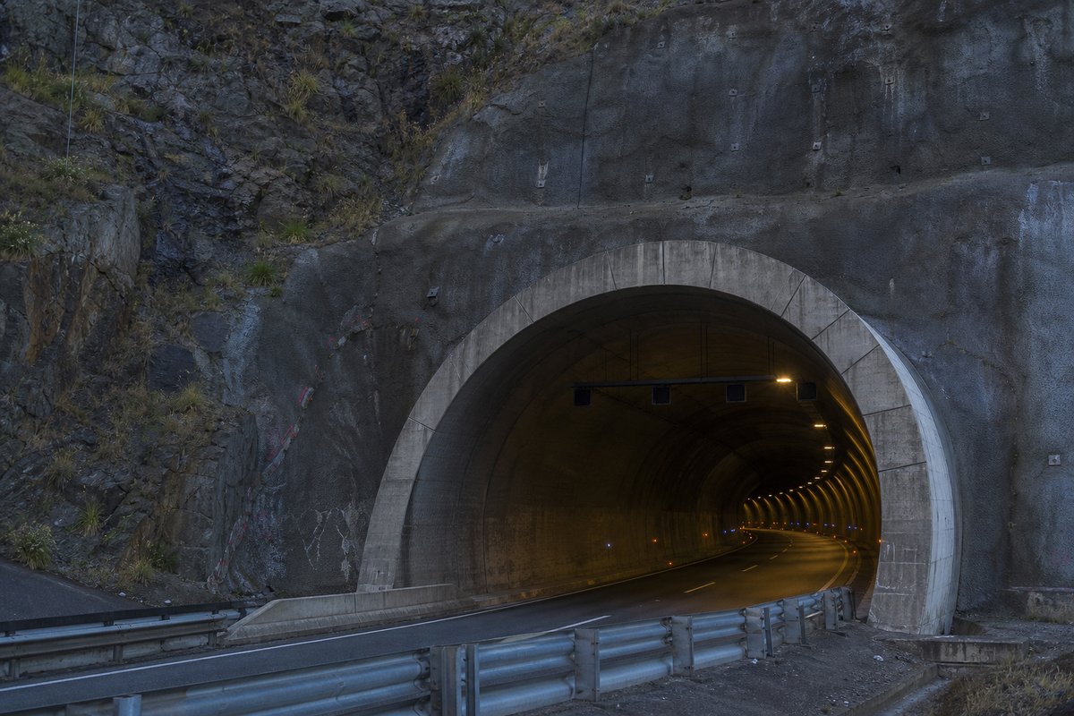 Road tunnel portal in Portugal: Atlantic granite hillside with a motorway tunnel mouth, in hard low winter sun, shot at 85mm from a distance. (AI-generated image)