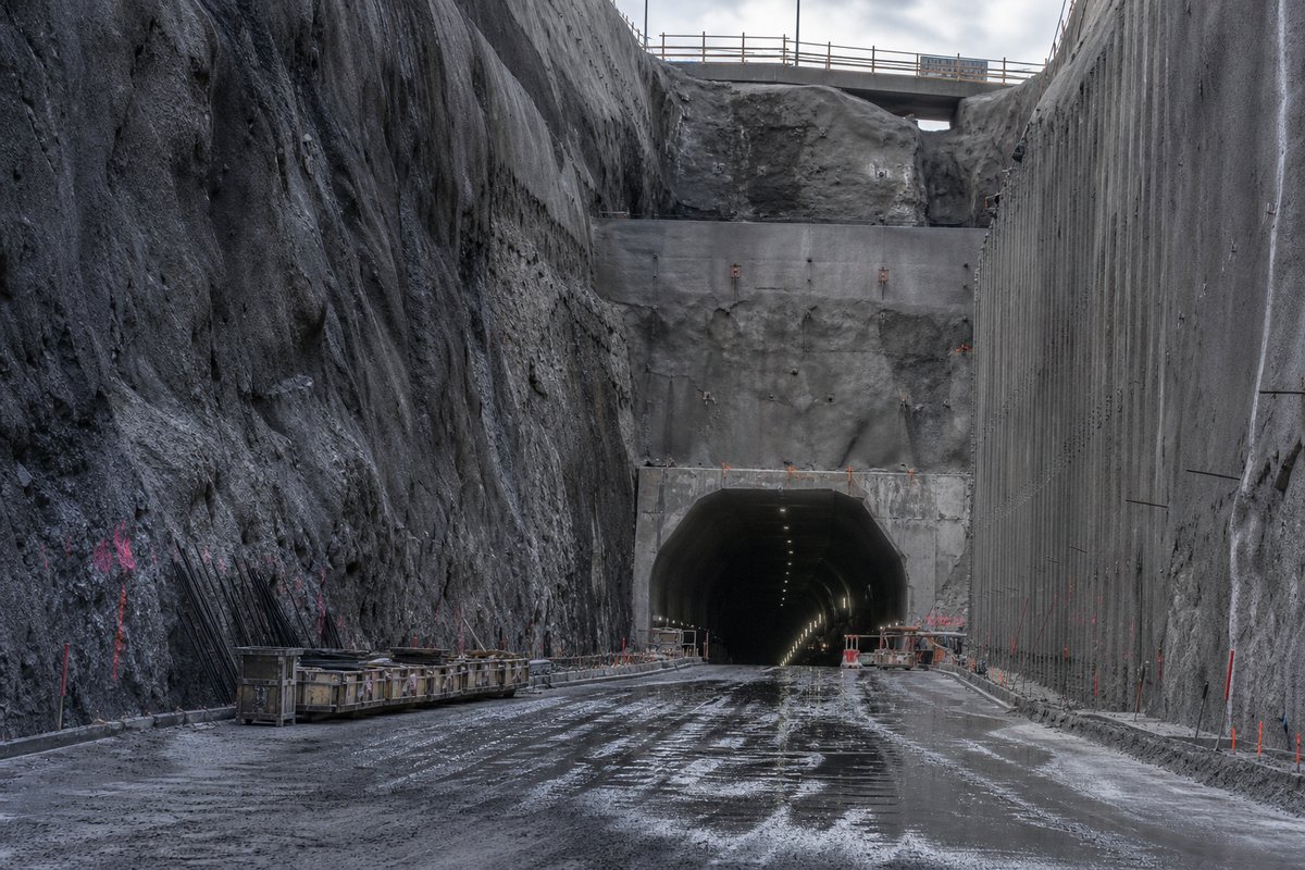 Heavy rock cutting leading to a tunnel portal, technical and unromantic: a mountainous transport corridor, in hard low winter sun, shot at 50mm. (AI-generated image)