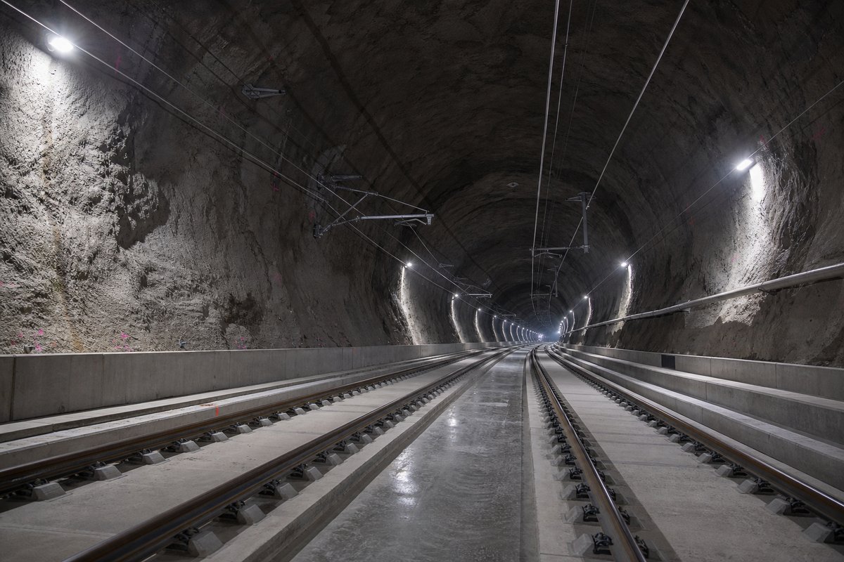 Double-track railway tunnel interior with ballastless slab track and catenary receding into darkness: a mountainous transport corridor, in hard low winter sun. (AI-generated image)