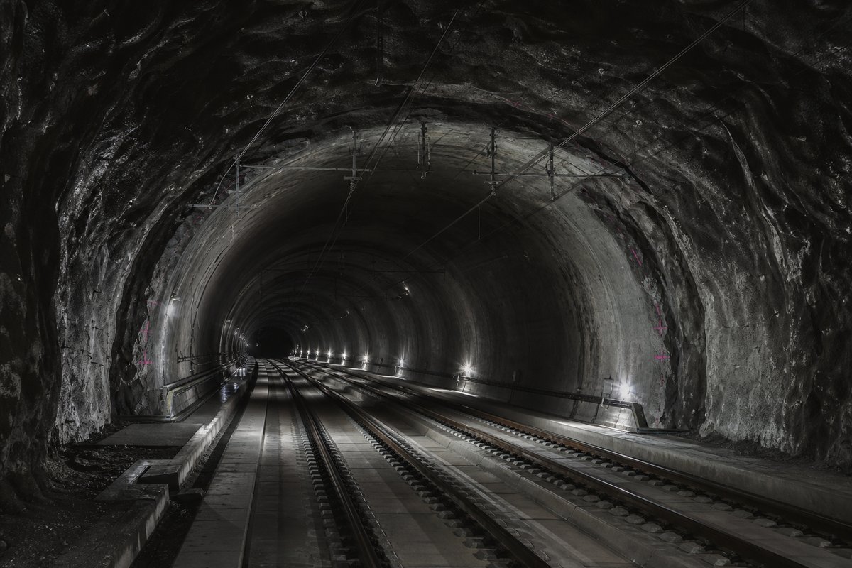 Double-track railway tunnel interior with ballastless slab track and catenary receding into darkness: a mountainous transport corridor, in drifting mist. (AI-generated image)