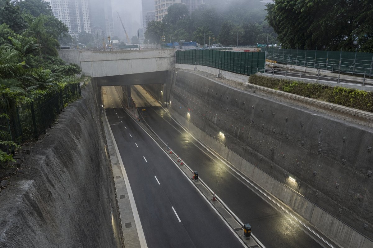 Road tunnel portal in Singapore: dense tropical city, the ramp down into an underground expressway, in drifting mist, a slightly elevated three-quarter view. (AI-generated image)