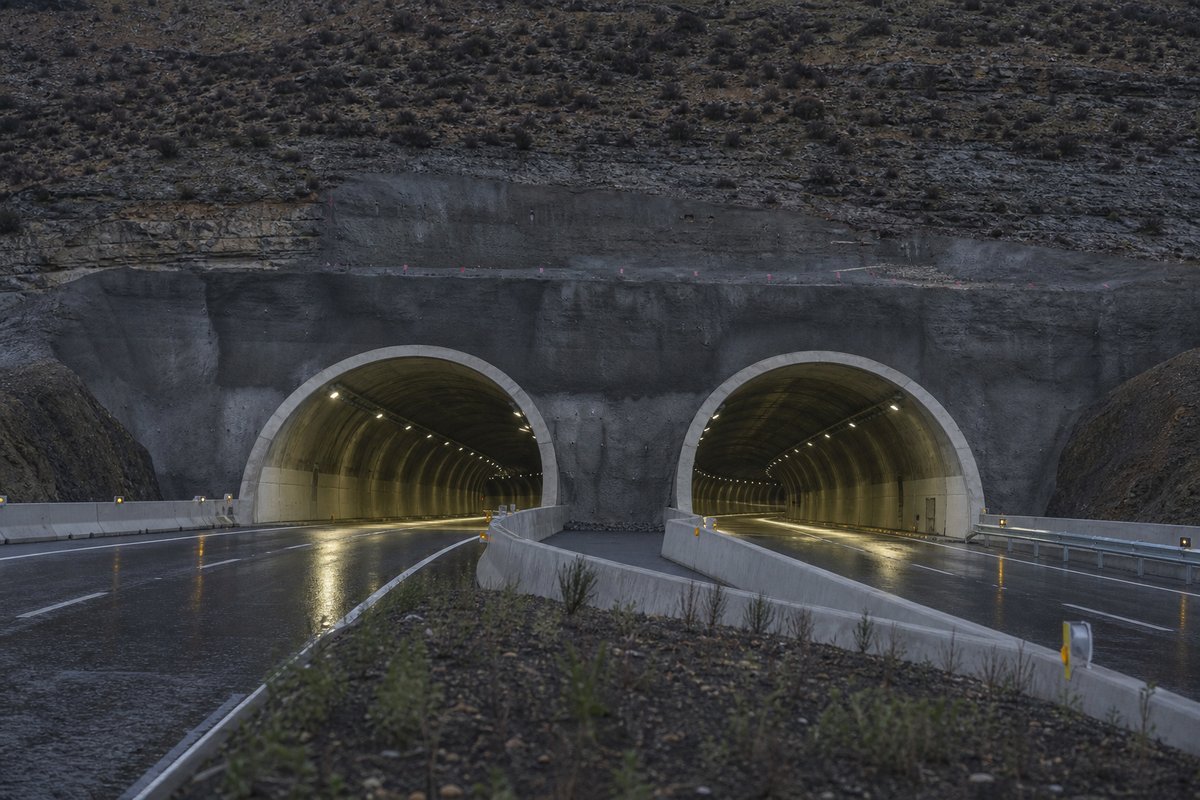 Road tunnel portal in Spain: arid meseta escarpment, a modern twin-bore motorway portal, after rain, everything wet and reflective, shot at 50mm, compressed. (AI-generated image)