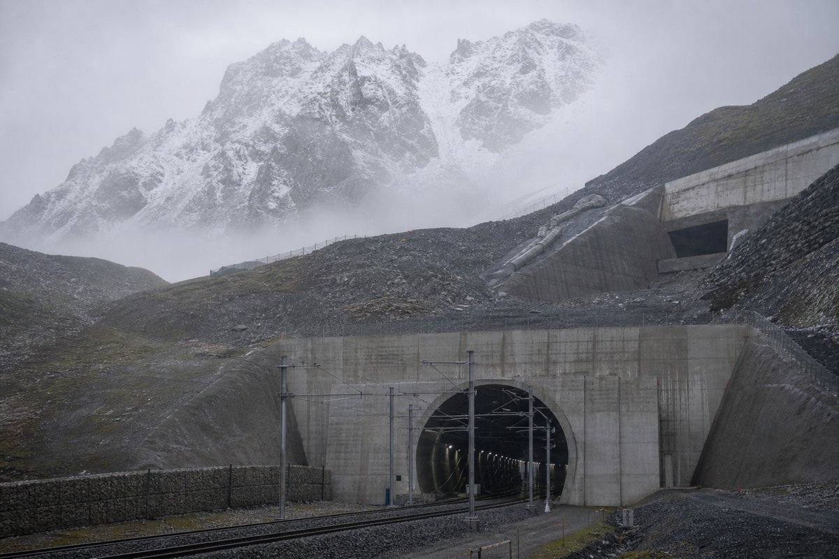 Railway tunnel portal with track running in in Switzerland: high alpine valley, snow on the crags above a massive base-tunnel portal, in thin morning fog. (AI-generated image)