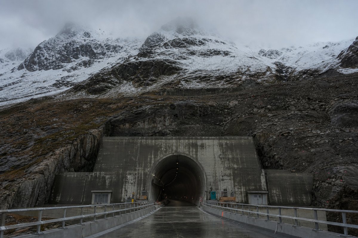 Transport infrastructure structure in Switzerland: high alpine valley, snow on the crags above a massive base-tunnel portal, under low grey cloud, shot at 35mm. (AI-generated image)