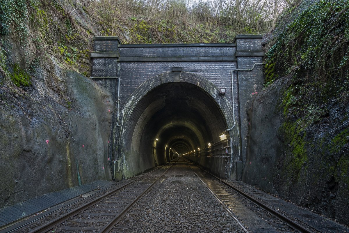 Railway tunnel portal with track running in in the United Kingdom: a mountainous transport corridor, in hard low winter sun, shot wide at 24mm. (AI-generated image)