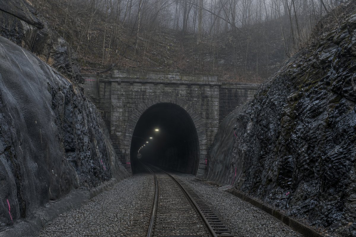 Railway tunnel portal with track running in in the United States: a mountainous transport corridor, in thin morning fog, shot at 85mm from a distance. (AI-generated image)