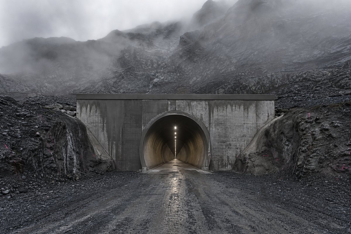 Transport infrastructure structure: a generic high mountain range with a very long tunnel portal, in drifting mist, a dead-centre symmetrical composition. (AI-generated image)