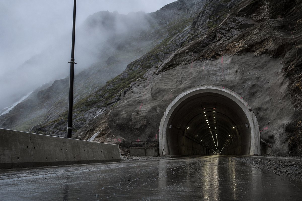 Transport infrastructure structure: a generic high mountain range with a very long tunnel portal, in drifting mist, a low camera position near the road surface. (AI-generated image)