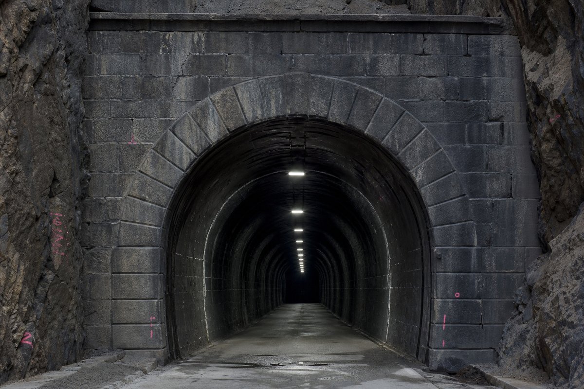 Nineteenth-century masonry tunnel portal with cut-stone voussoirs, soot-darkened and weathered, in cold clear light, shot at 50mm, compressed. (immagine generata con AI)