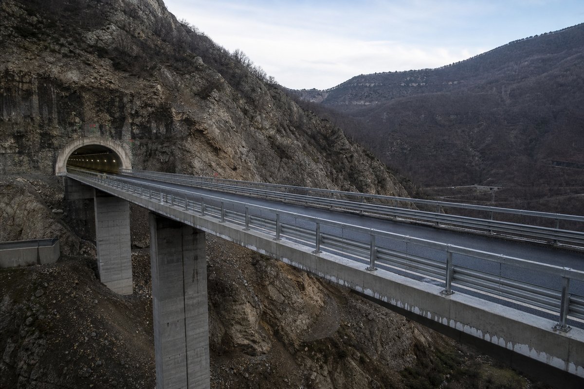 Italian motorway viaduct running straight into a mountain portal on an Apennine ridge, in cold clear light, shot wide at 24mm. (immagine generata con AI)