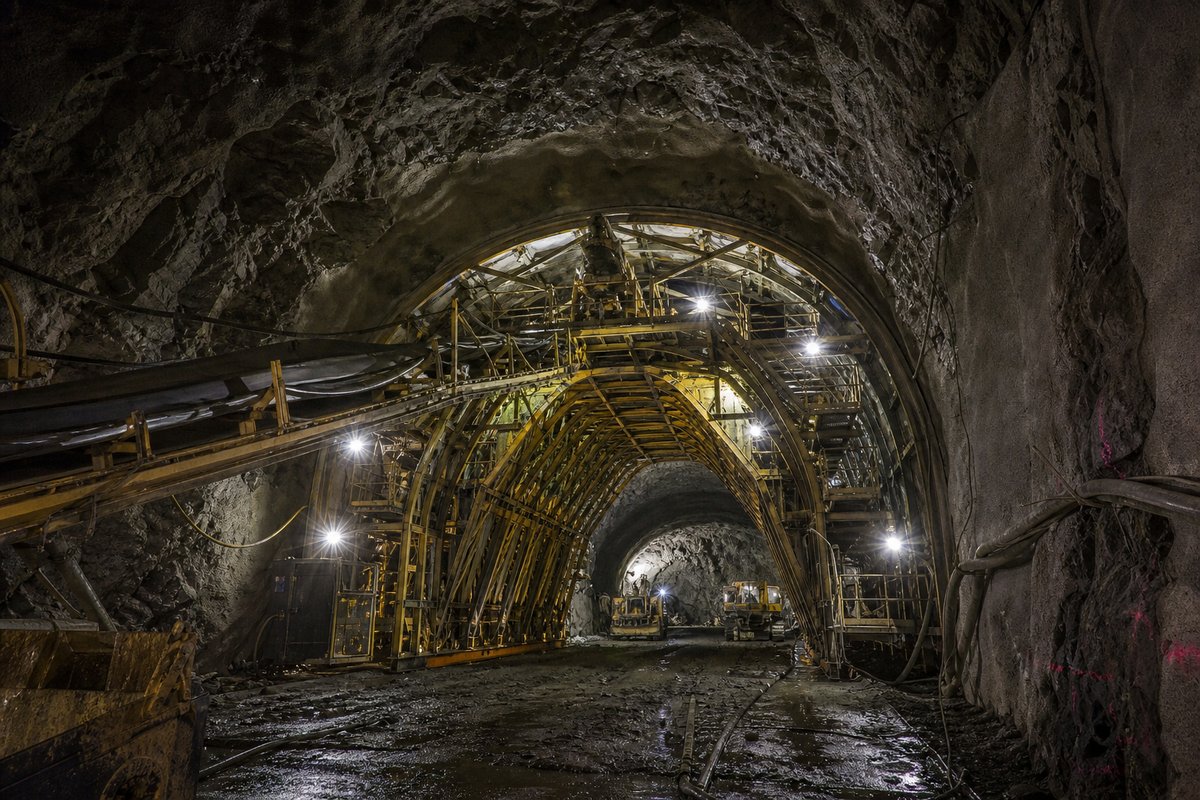 Tunnel construction site at night, portal formwork and site lighting, spoil conveyors running. (AI-generated image)