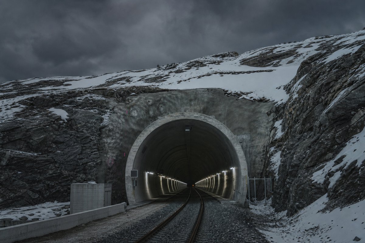 Norwegian railway tunnel portal in glaciated bedrock with snow on the cutting slopes, under a heavy dark sky, shot at 50mm, compressed. (bilete generert med AI)