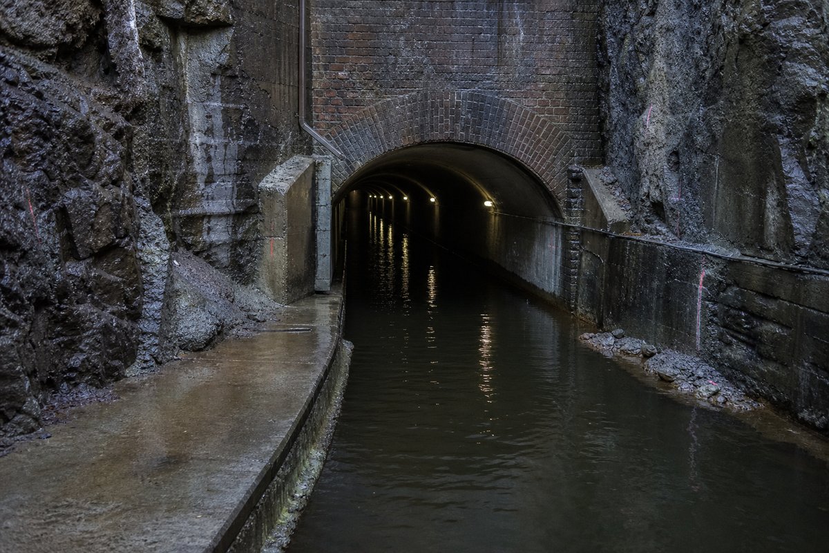 Narrow historic navigation tunnel entrance over black water, brick arch, no boats, after rain, everything wet and reflective, shot at 35mm. (bilete generert med AI)