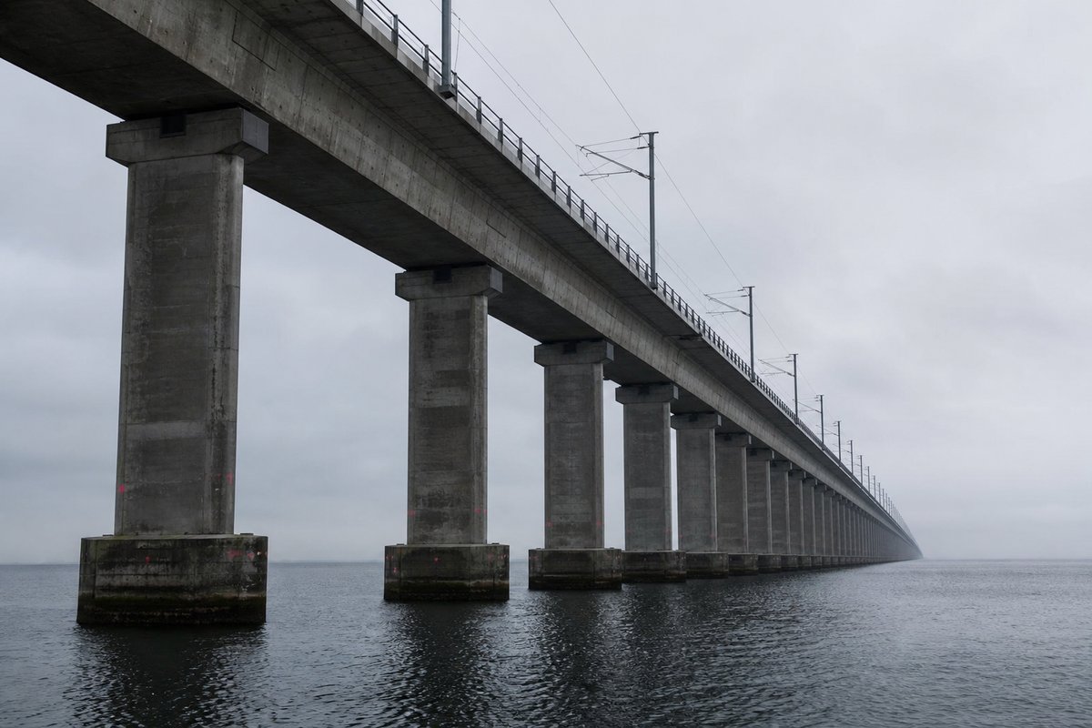 Very long low railway viaduct on hundreds of identical concrete piers marching across flat water into the mist, seen from below at the waterline. (AI-generated image)