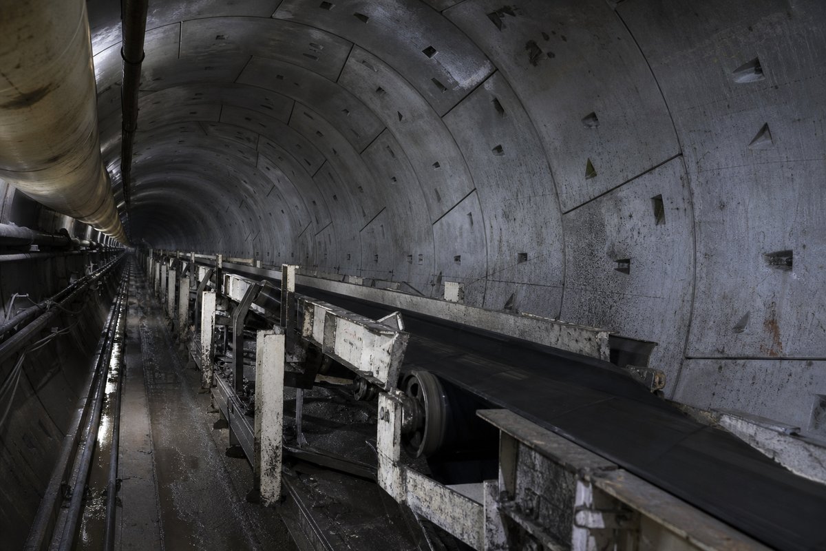 Trailing gantries of a tunnel boring machine inside a completed segmental lining, conveyor running back, receding into darkness. (AI-generated image)