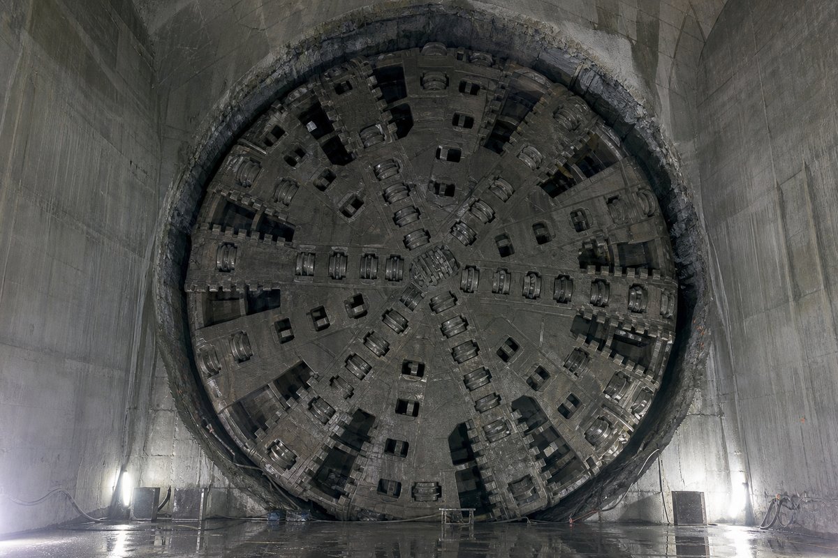 Cutterhead of an enormous tunnel boring machine seen head-on in a launch chamber, disc cutters and spokes, worklights from below. (AI-generated image)